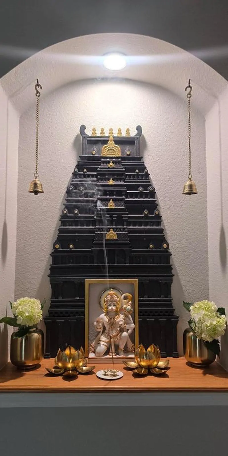 Rawdius Gopuram Customer Installation Black gopuram wall decor backdrop behind a framed Hanuman idol inside an arched white pooja niche