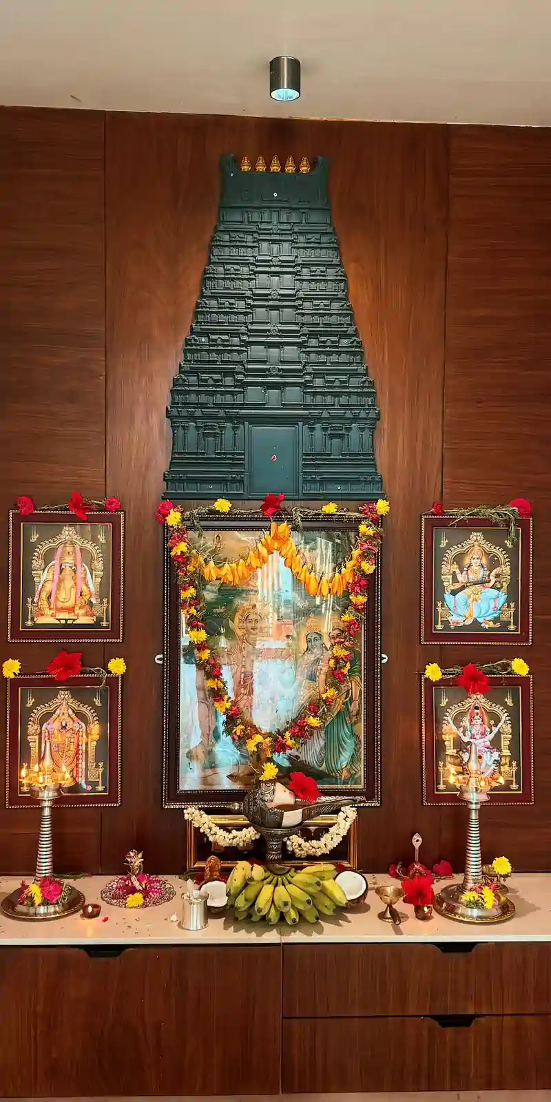 Rawdius Gopuram Customer Installation Dark green gopuram wall art mounted above framed deity photos on a wooden pooja wall