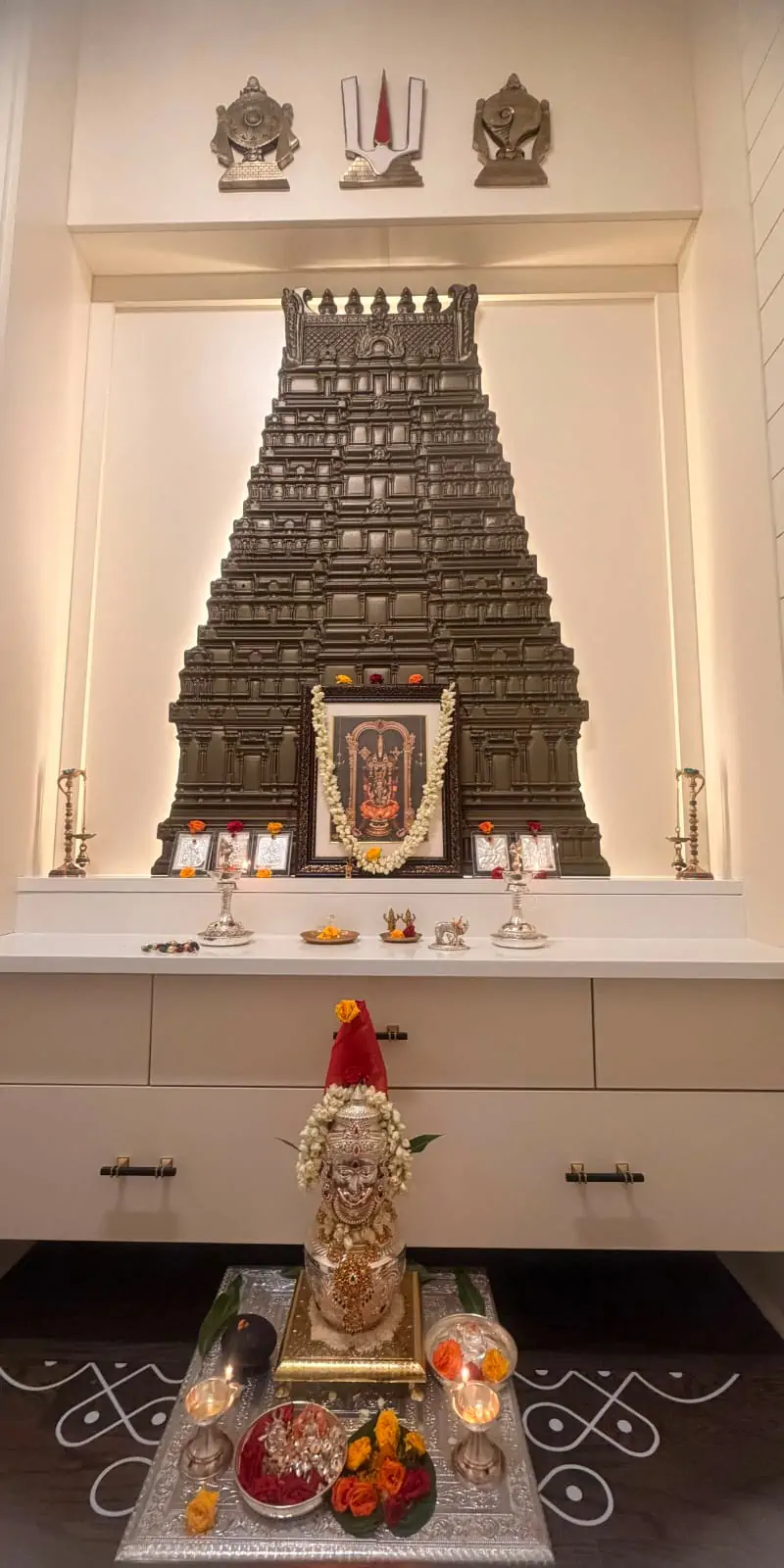 Rawdius Gopuram Customer Installation Dark grey gopuram art backdrop in a white pooja niche with sacred symbols above