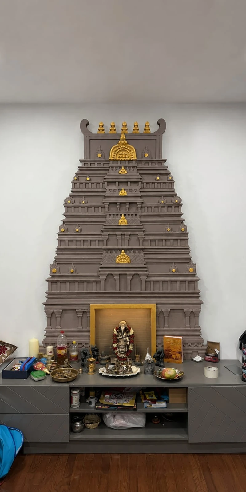 Rawdius Gopuram Customer Installation Dark grey gopuram decor mounted above a long grey media console displaying brass pooja items