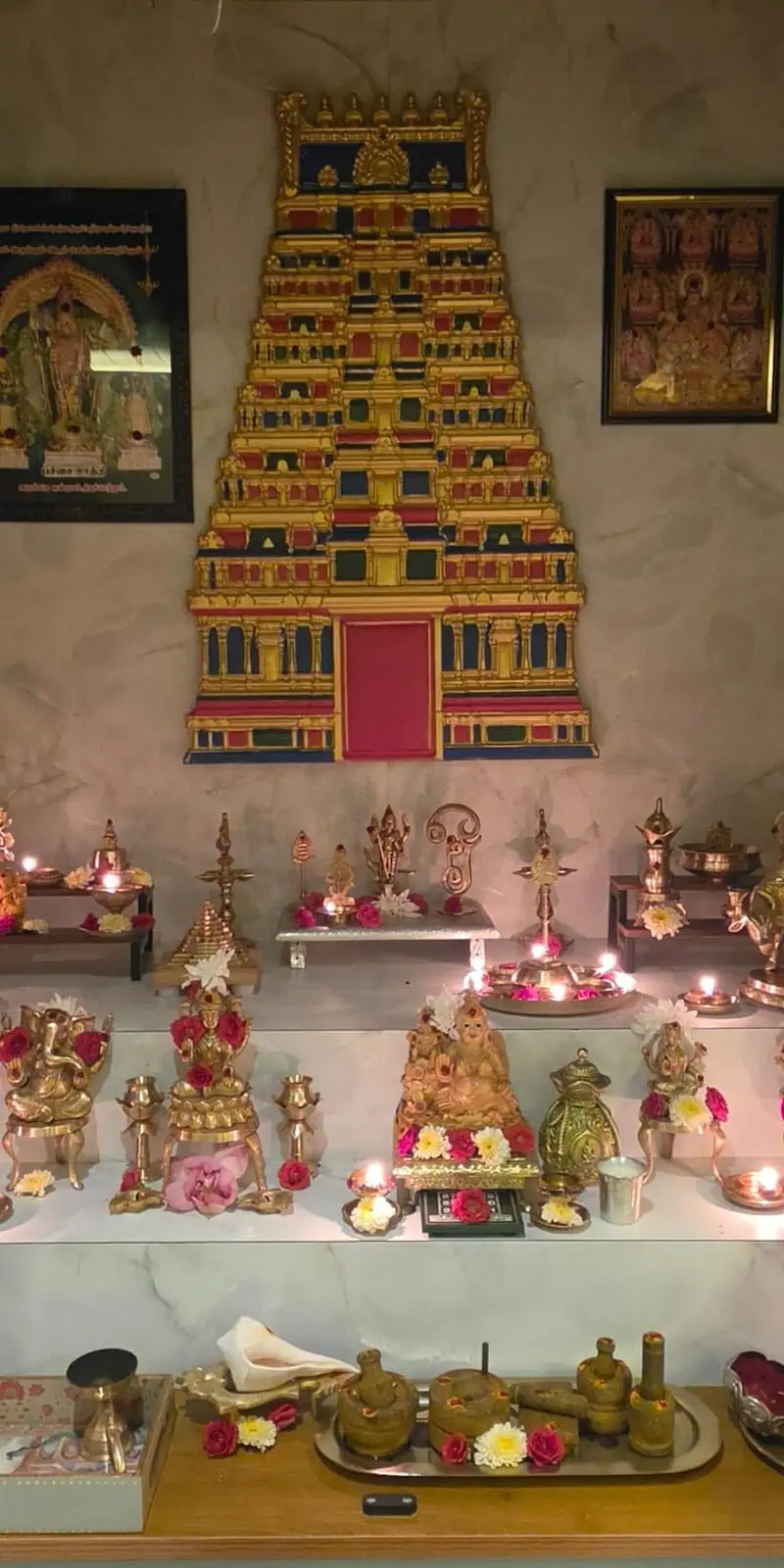 Rawdius Gopuram Customer Installation Gold, blue, and red gopuram art mounted above brass deity idols on a multi tiered pooja altar