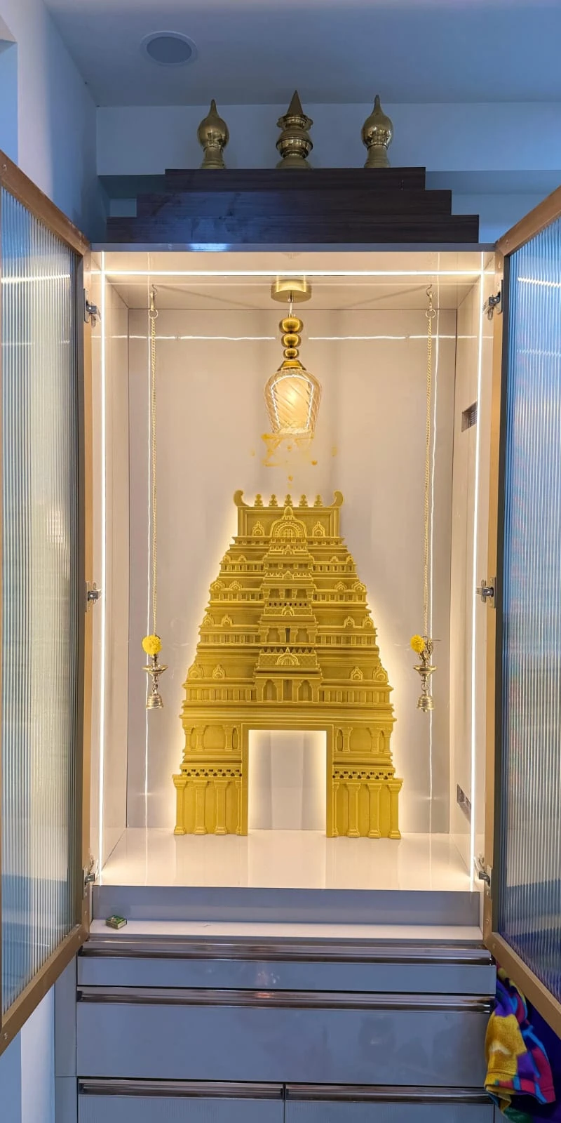 Rawdius Gopuram Customer Installation Golden temple gopuram backdrop installed inside an illuminated glass door pooja cabinet