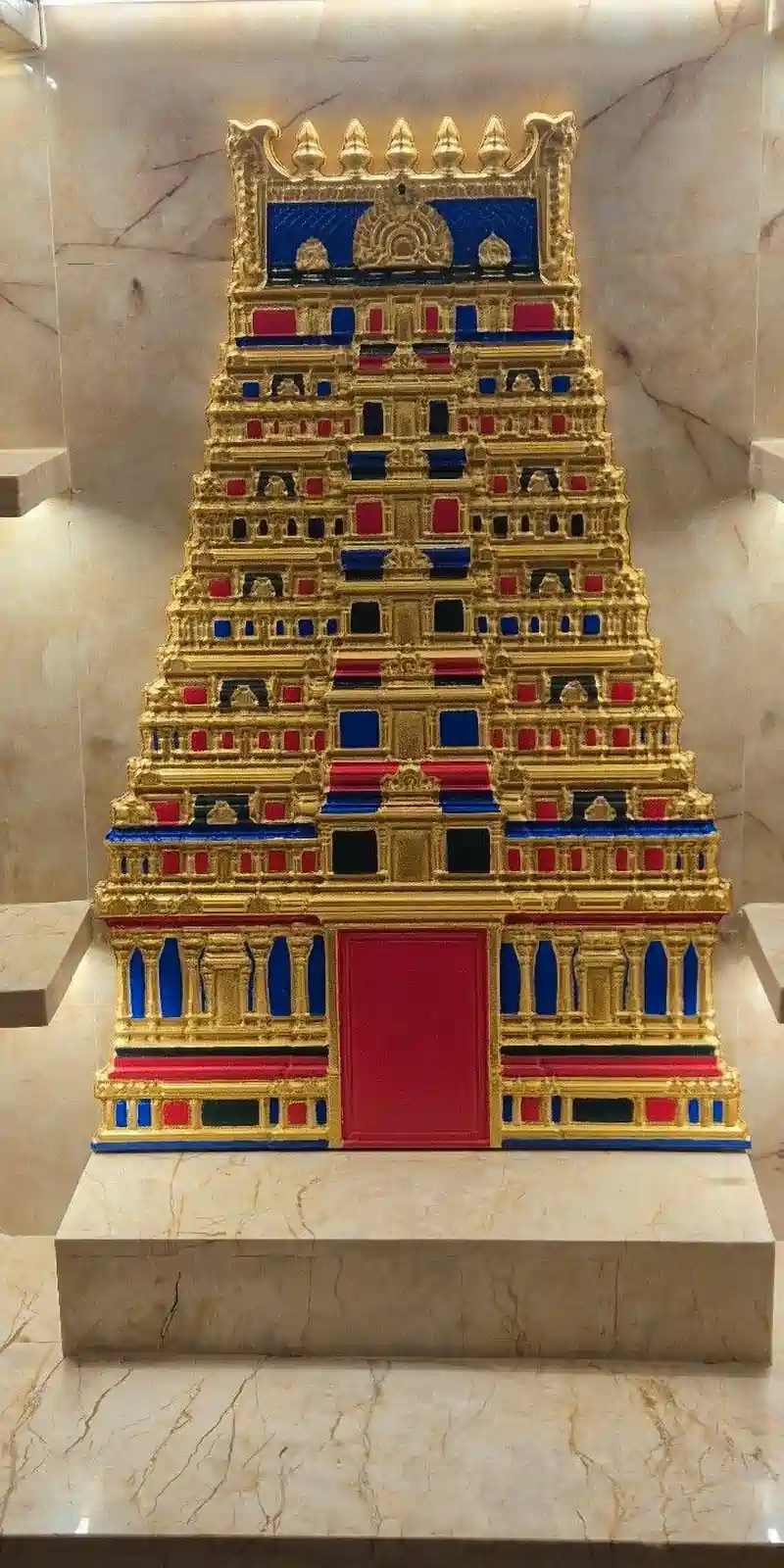 Rawdius Gopuram Customer Installation Ornate gold, blue, and red temple gopuram art mounted inside a marble pooja alcove